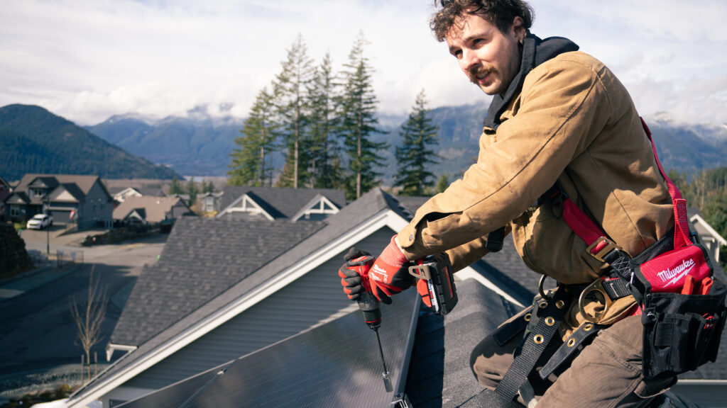 Skilled solar contractor securing a photovoltaic panel to a roof rack with a drill to ensure a weather-resistant energy setup.